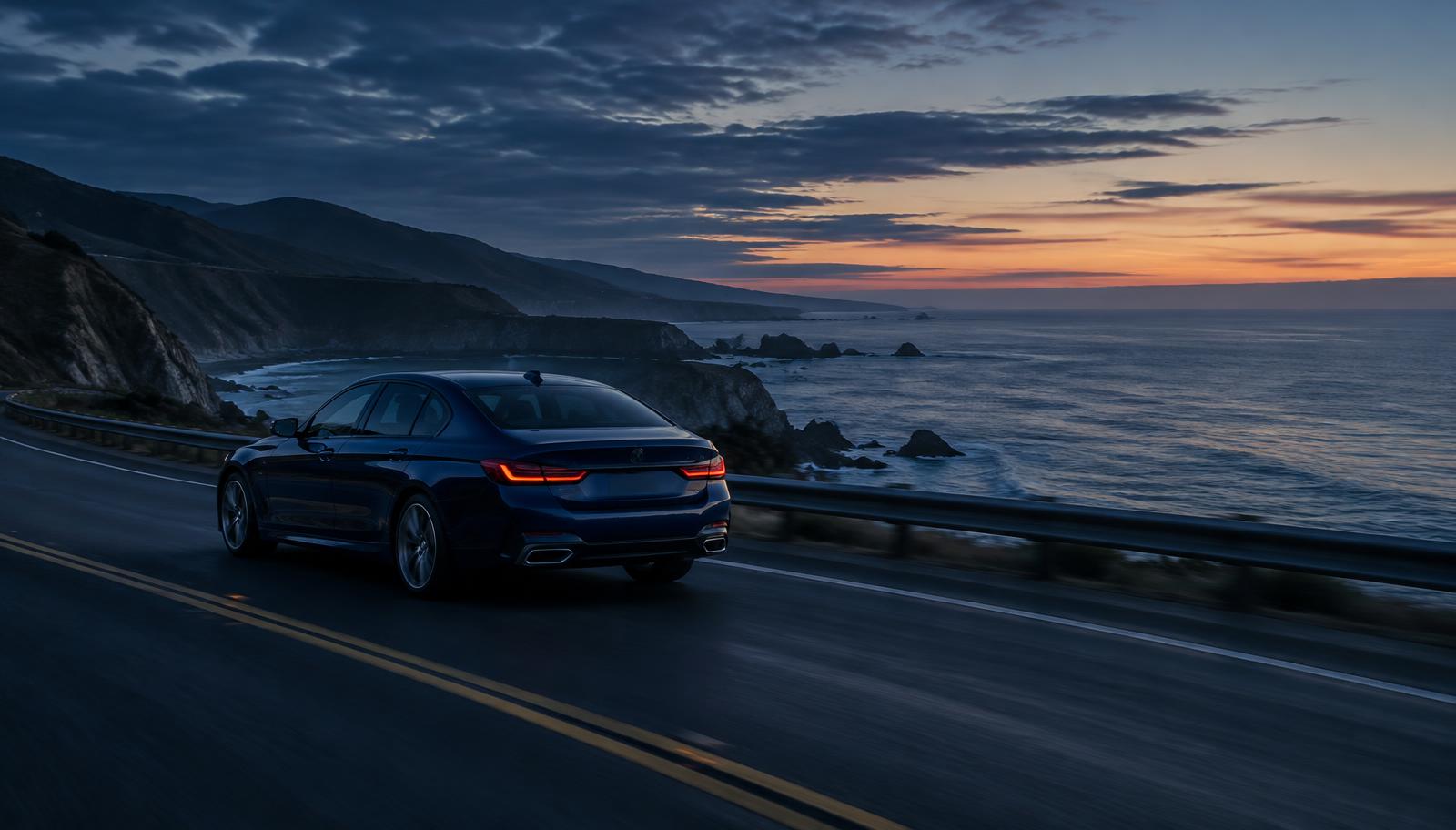 A dark blue saloon car driving along a coastal road at dusk